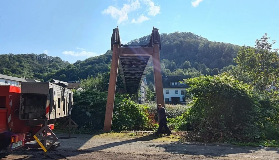 Alte Eisenbahnbrücke vor bewaldetem Hügel bei sonnigem Wetter.