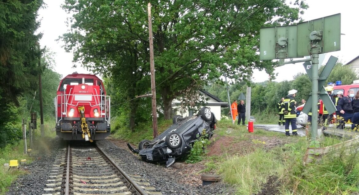 Zug nähert sich einem verunglückten Auto neben den Gleisen.
