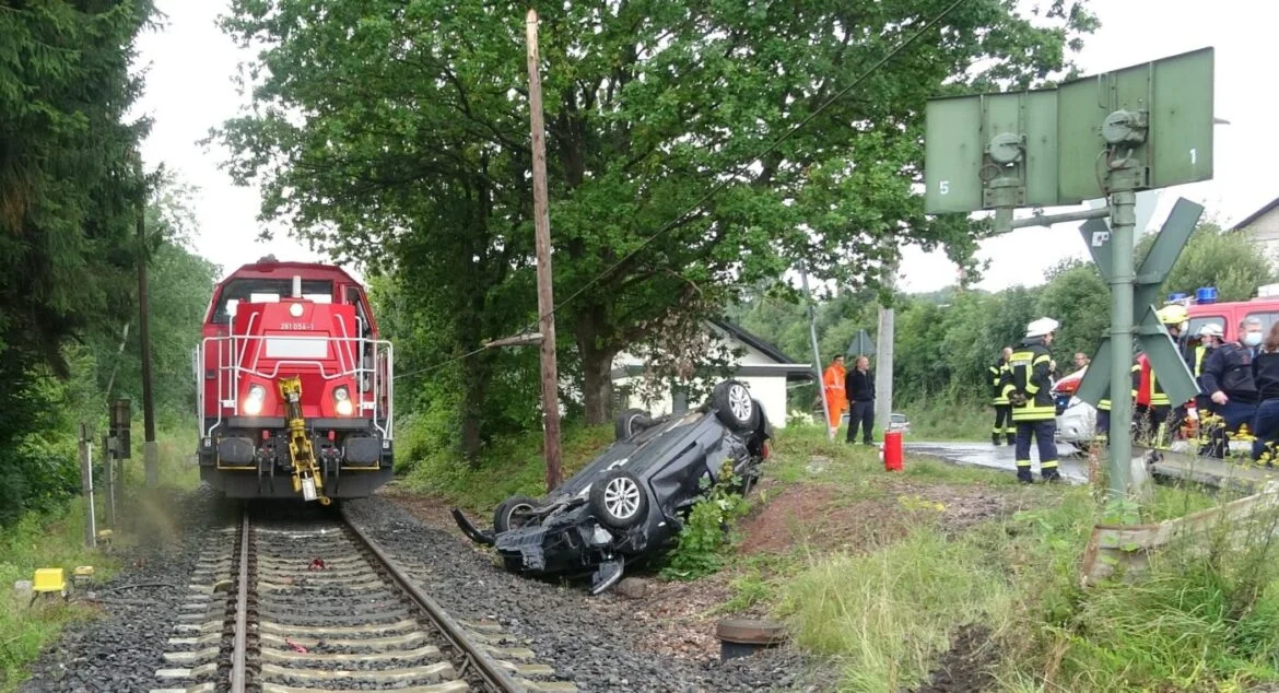 Zug nähert sich einem verunglückten Auto neben den Gleisen.
