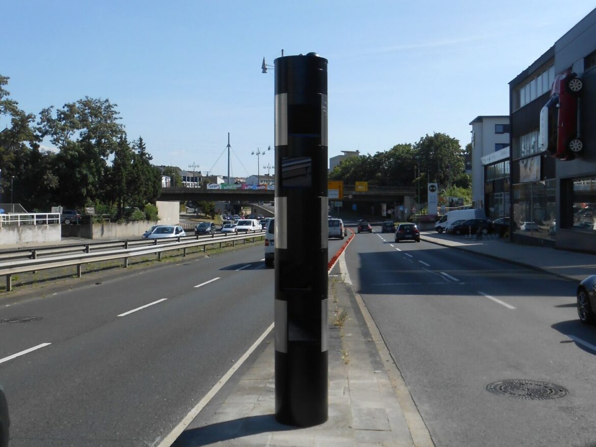 Verkehrskamera auf einer Straße mit Autos und Gebäuden im Hintergrund.