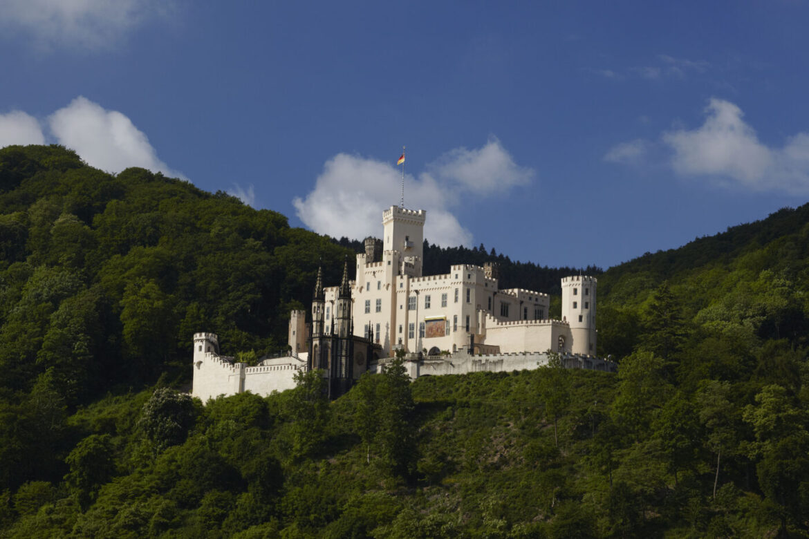 Burg Stolzenfels auf einem bewaldeten Hügel unter blauem Himmel
