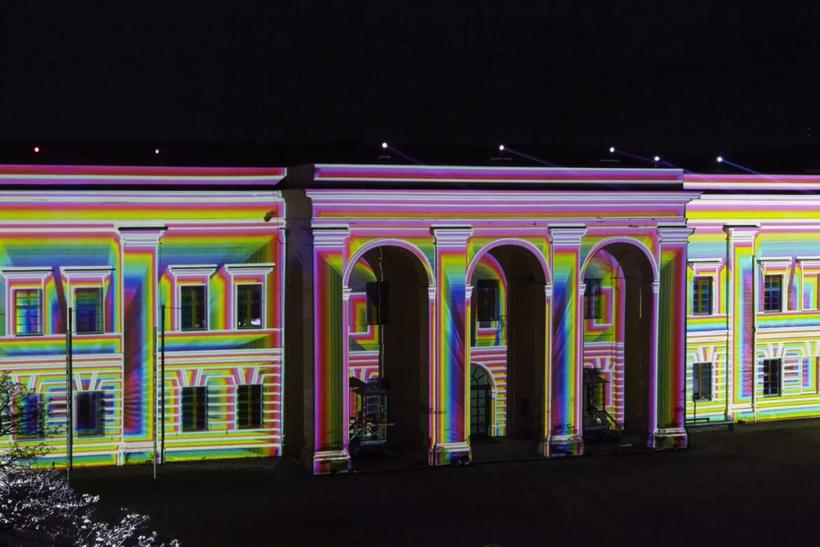 Bunte Lichtprojektionen auf einem historischen Gebäude bei Nacht.