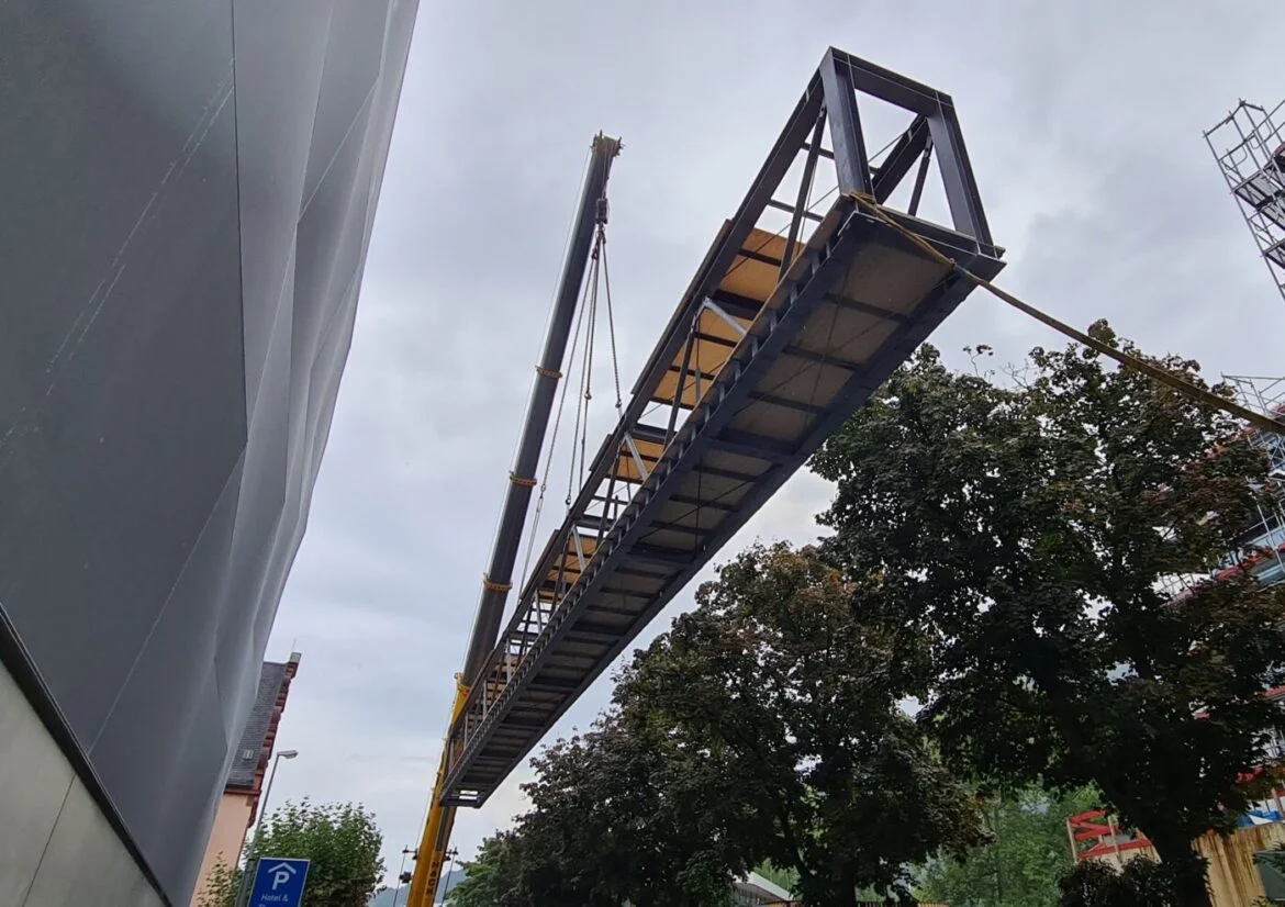 Kran hebt eine große Metallstruktur neben einem Gebäude.