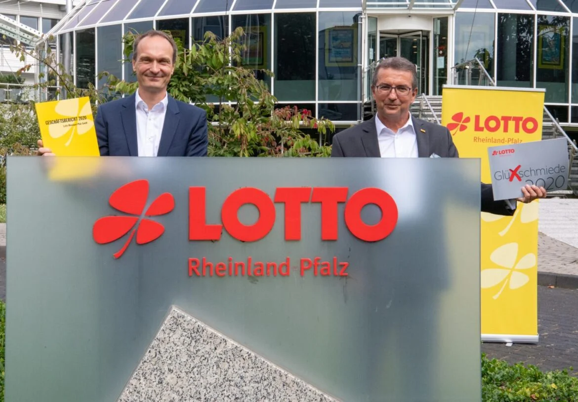Zwei Männer halten Broschüren vor dem Lotto Rheinland-Pfalz Gebäude.