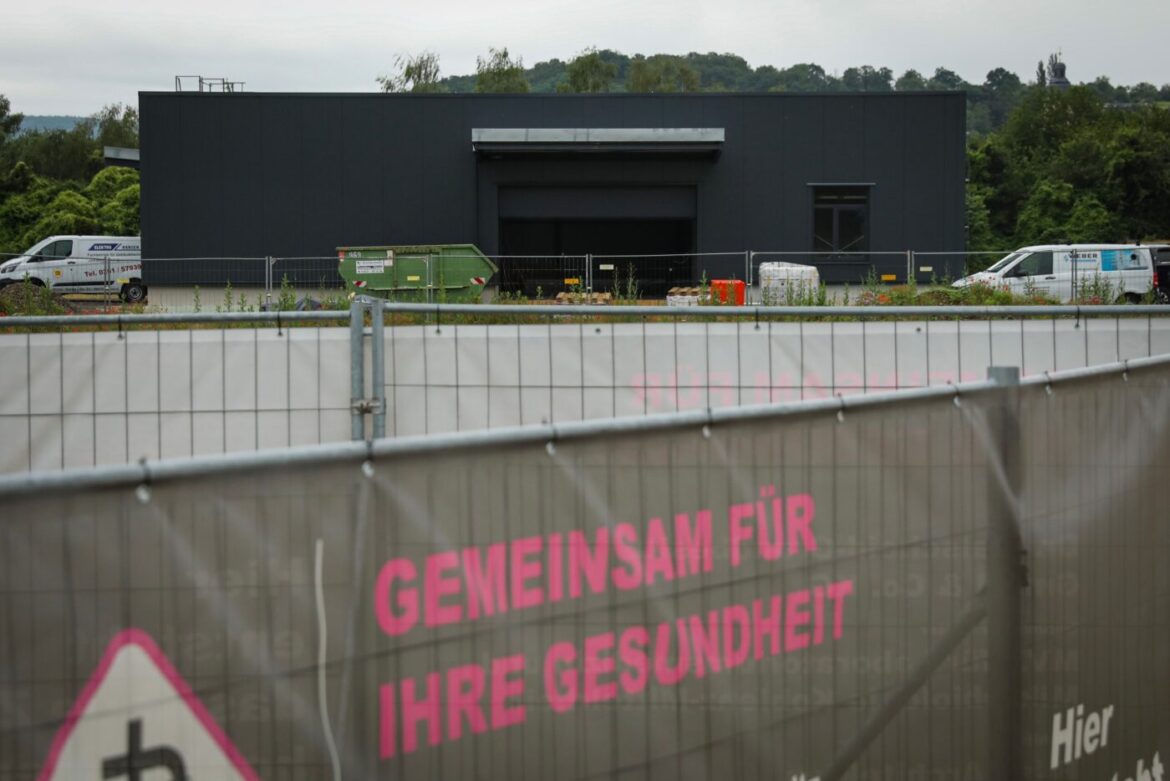 Graues Gebäude hinter einem Bauzaun mit der Aufschrift 'Gemeinsam für Ihre Gesundheit'.