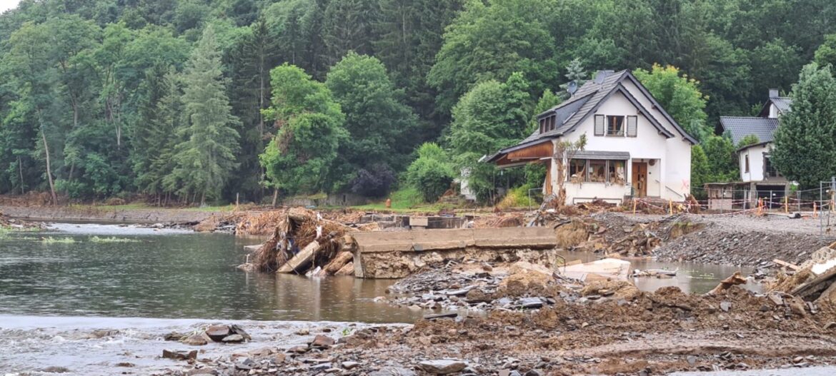 Hochwasserschäden an einem Haus am Flussufer mit umgestürzten Bäumen.