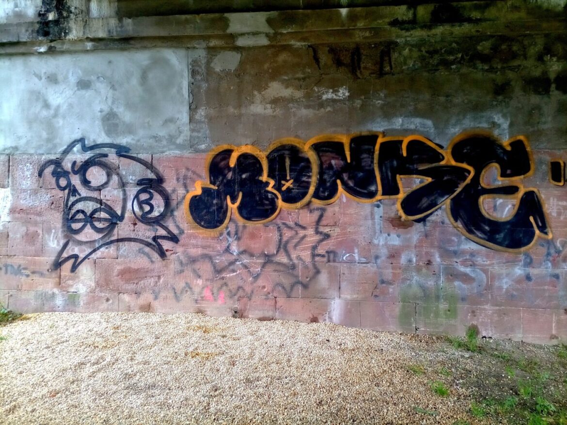 Graffiti an einer Betonwand unter einer Brücke.