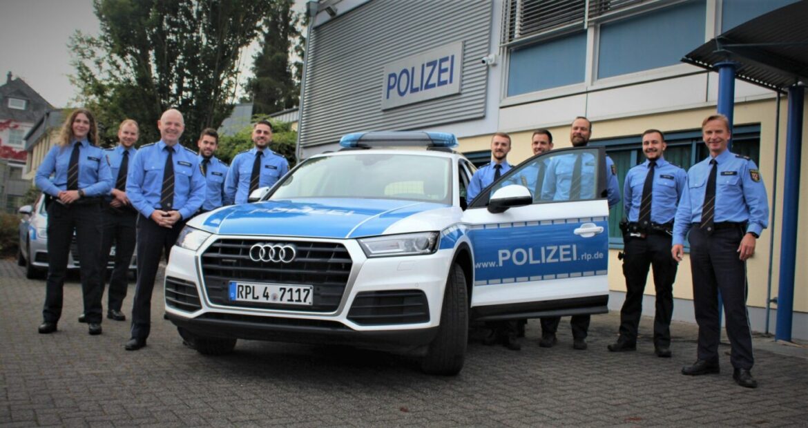 Polizeibeamte stehen vor einem Polizeiauto vor einer Wache.