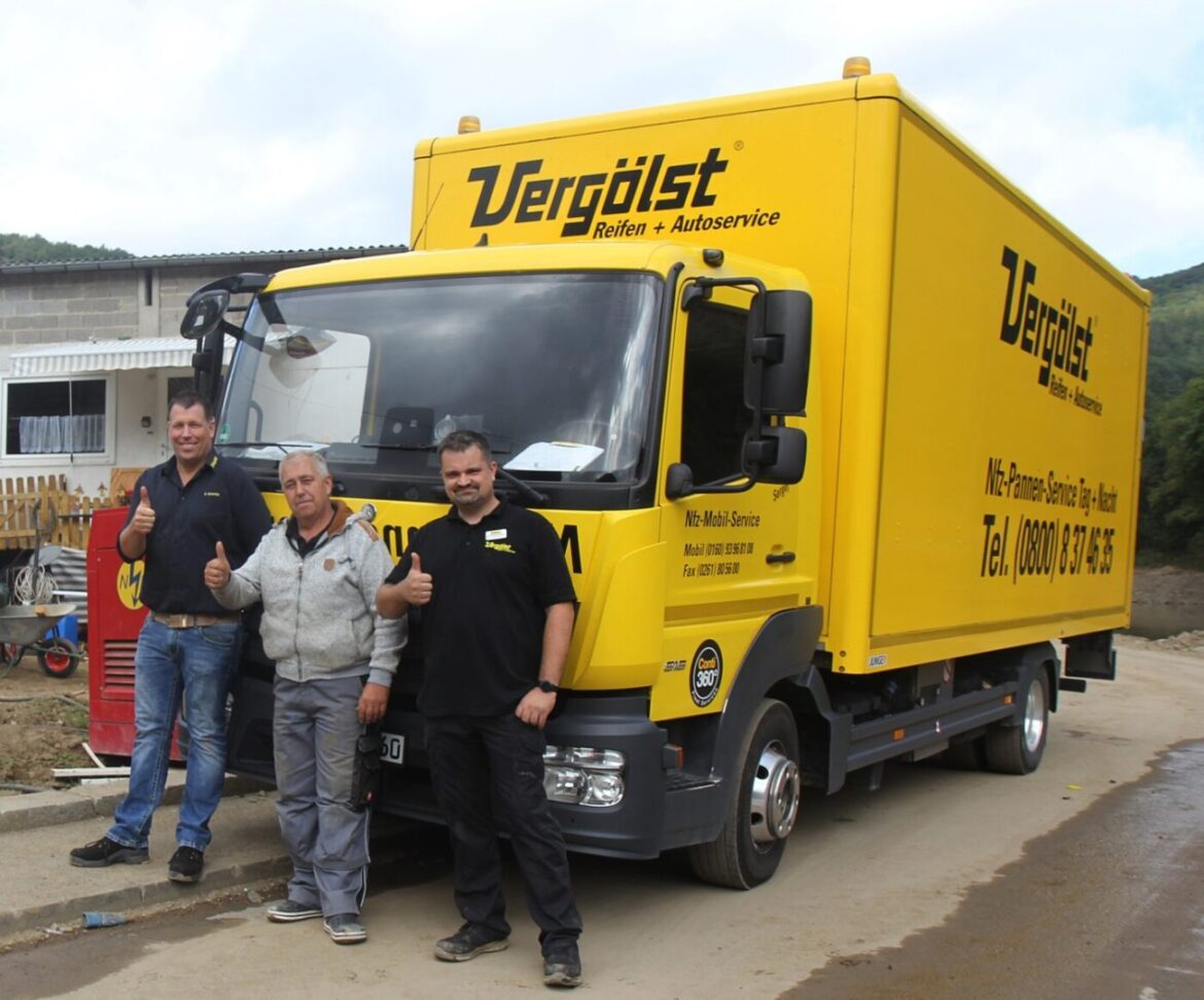 Drei Männer stehen vor einem gelben LKW mit Daumen hoch.