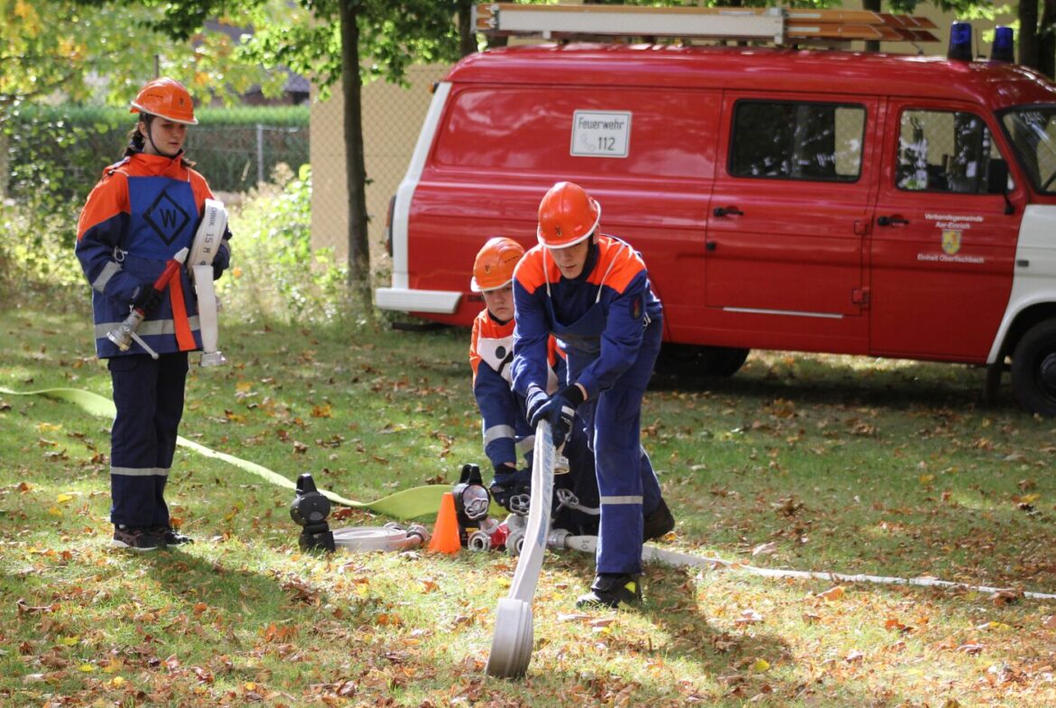 Jugendliche Feuerwehrleute üben mit einem Schlauch im Freien.