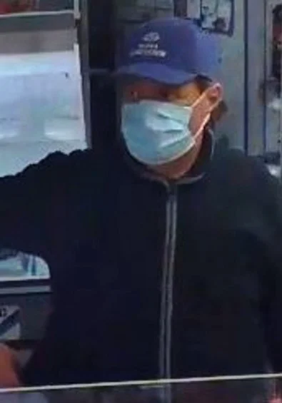 Person mit blauer Kappe und Maske in einem Geschäft