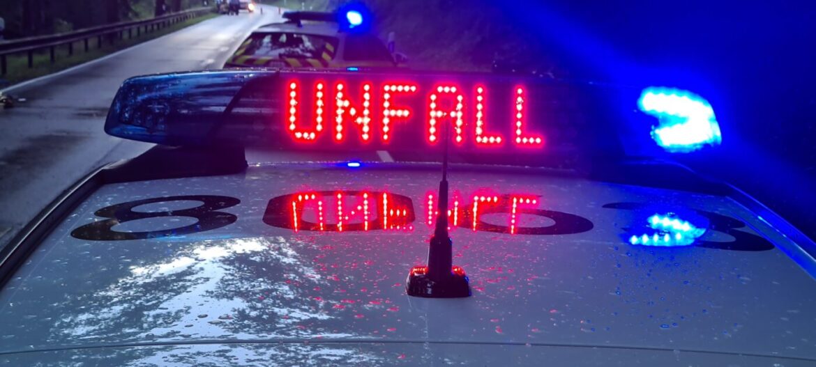 Polizeiauto mit Unfallwarnung und Blaulicht auf einer nassen Straße.