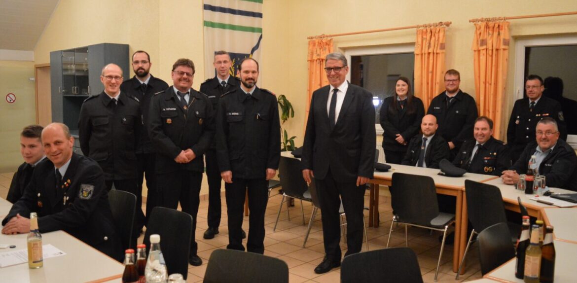 Gruppe von Feuerwehrleuten und einem Anzugträger in einem Versammlungsraum.