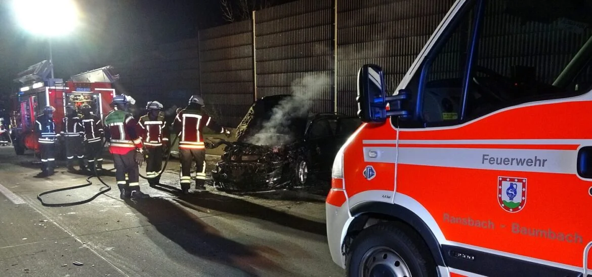 Feuerwehr löscht brennendes Auto auf Autobahn bei Nacht.
