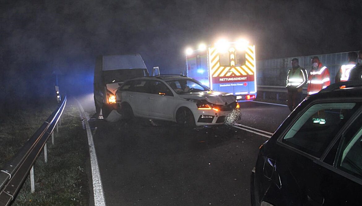 Autounfall auf einer Landstraße bei Nacht mit Rettungsfahrzeug im Hintergrund.