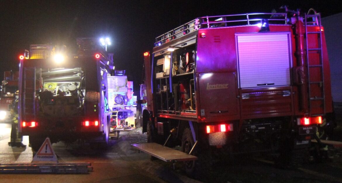 Feuerwehrfahrzeuge bei Nacht im Einsatz mit blinkenden Lichtern.