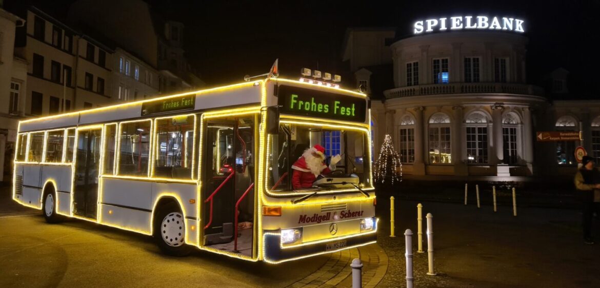 Weihnachtsbus mit Lichtern und Weihnachtsmann vor einem Gebäude.