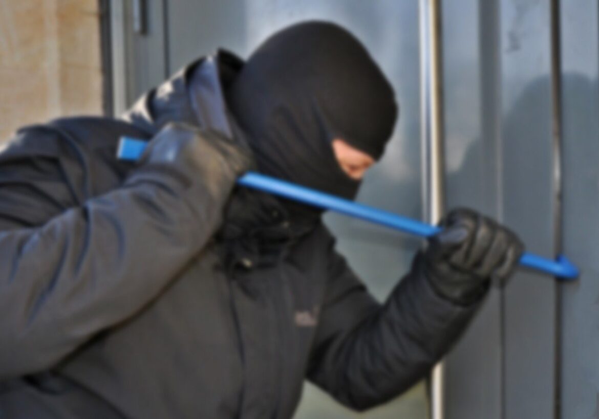 Verschleierter Einbrecher versucht, eine Tür mit Brecheisen zu öffnen.