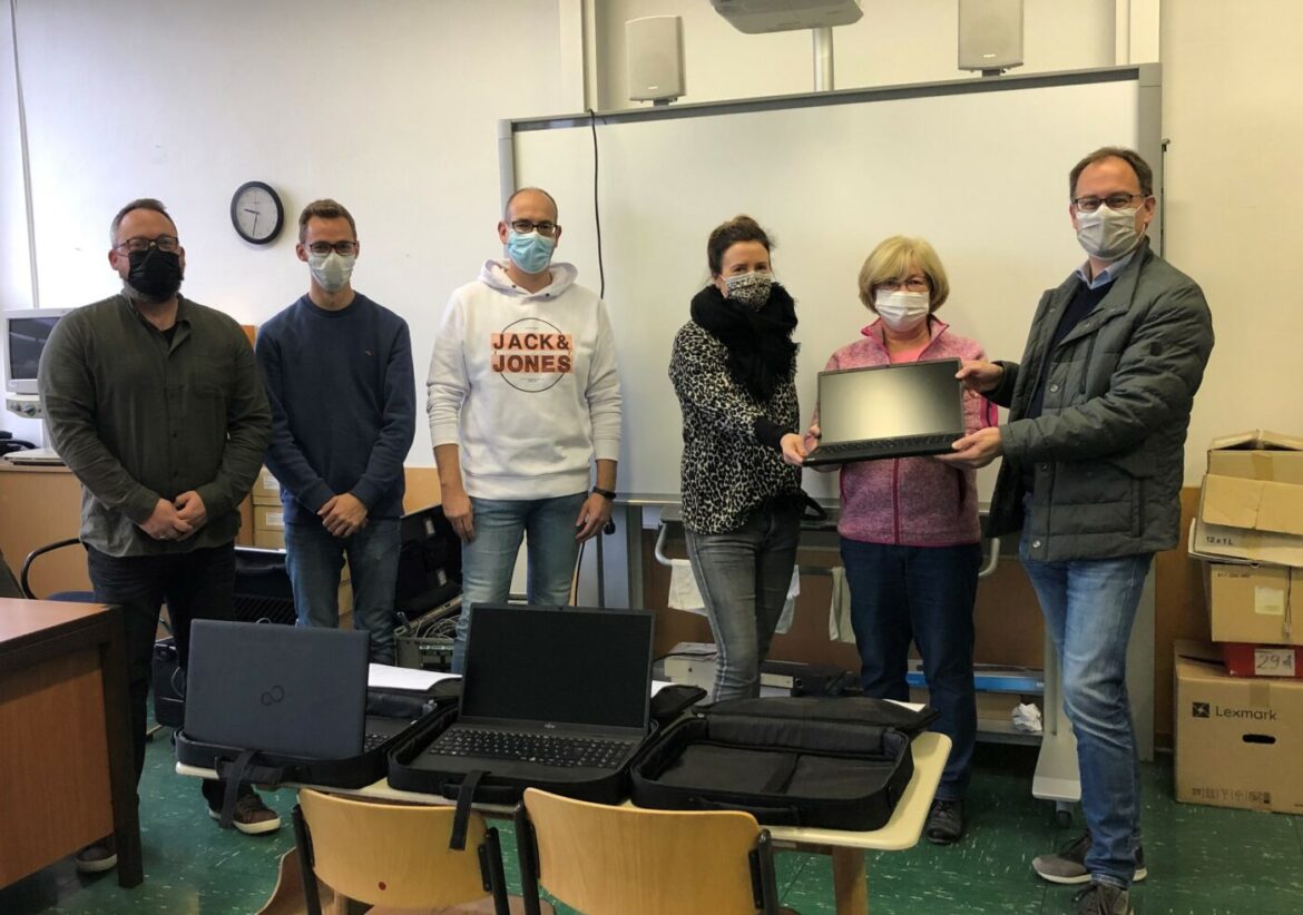 Sechs Personen präsentieren Laptops in einem Klassenzimmer.