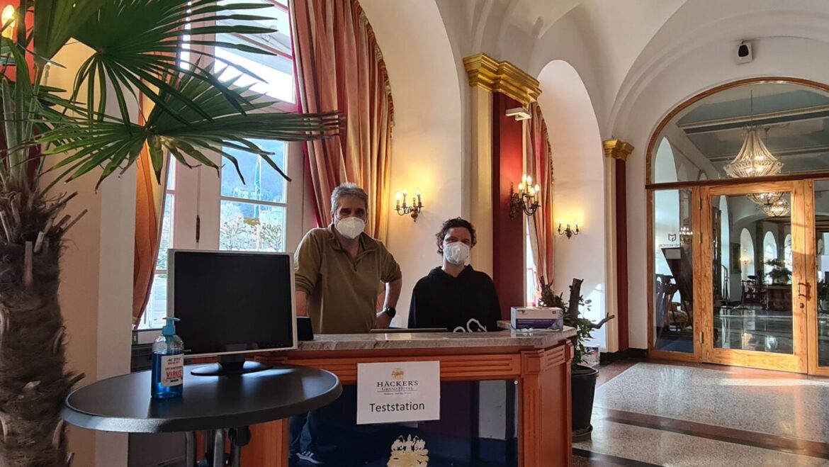 Zwei Personen mit Masken an einer Teststation in einem eleganten Raum.