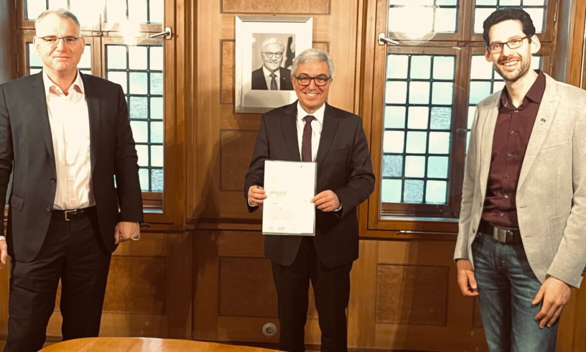 Drei Männer in einem Raum, einer hält ein Dokument in der Hand.