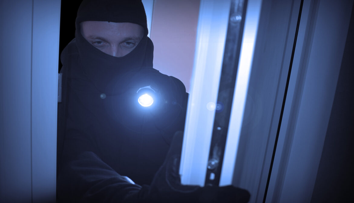 Einbrecher mit Taschenlampe in dunklem Raum