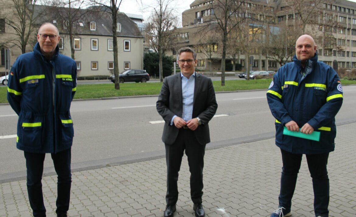 Drei Männer stehen auf einem Bürgersteig vor einer Straße.