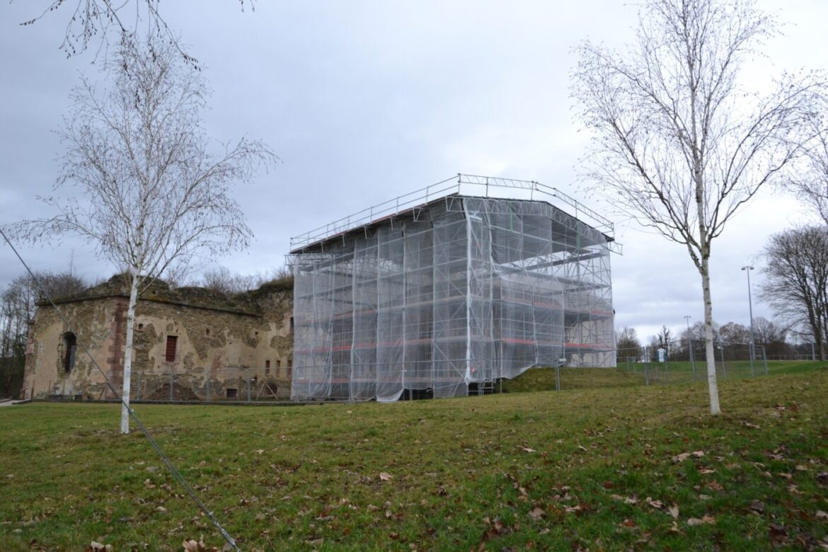 Historisches Gebäude mit Gerüst und Schutzplane, Bäume im Vordergrund.