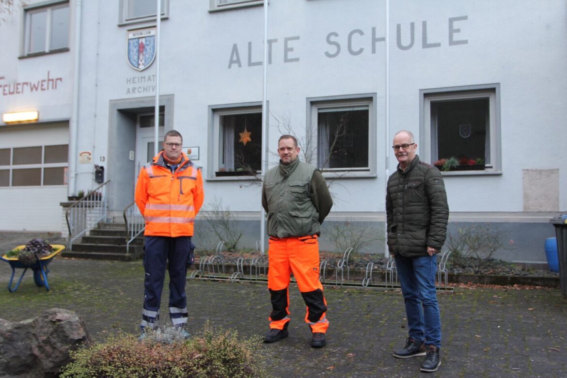 Drei Männer in Arbeitskleidung vor einem Gebäude mit der Aufschrift 'Alte Schule'.