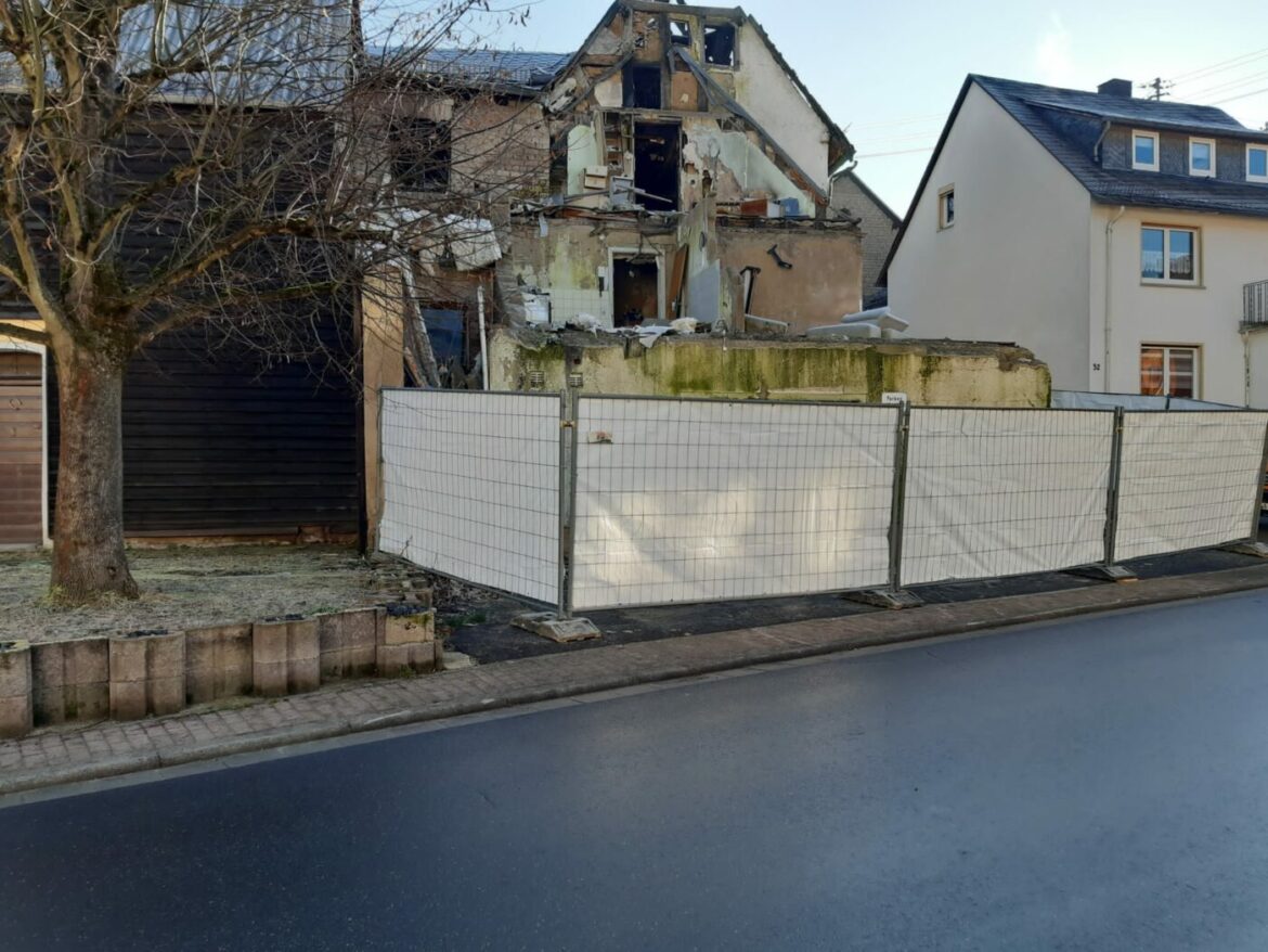 Teilweise zerstörtes Haus in Arzbach hinter einem Bauzaun.