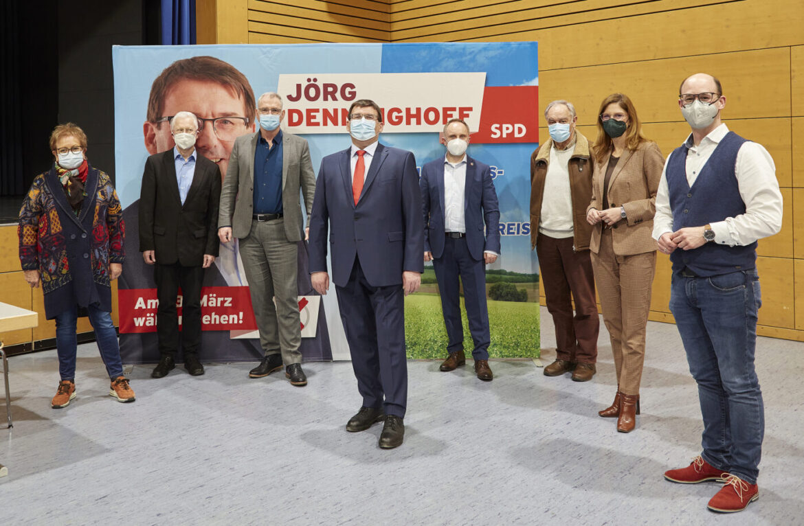 Gruppe von Menschen bei einer Mitgliederversammlung mit Plakat im Hintergrund.