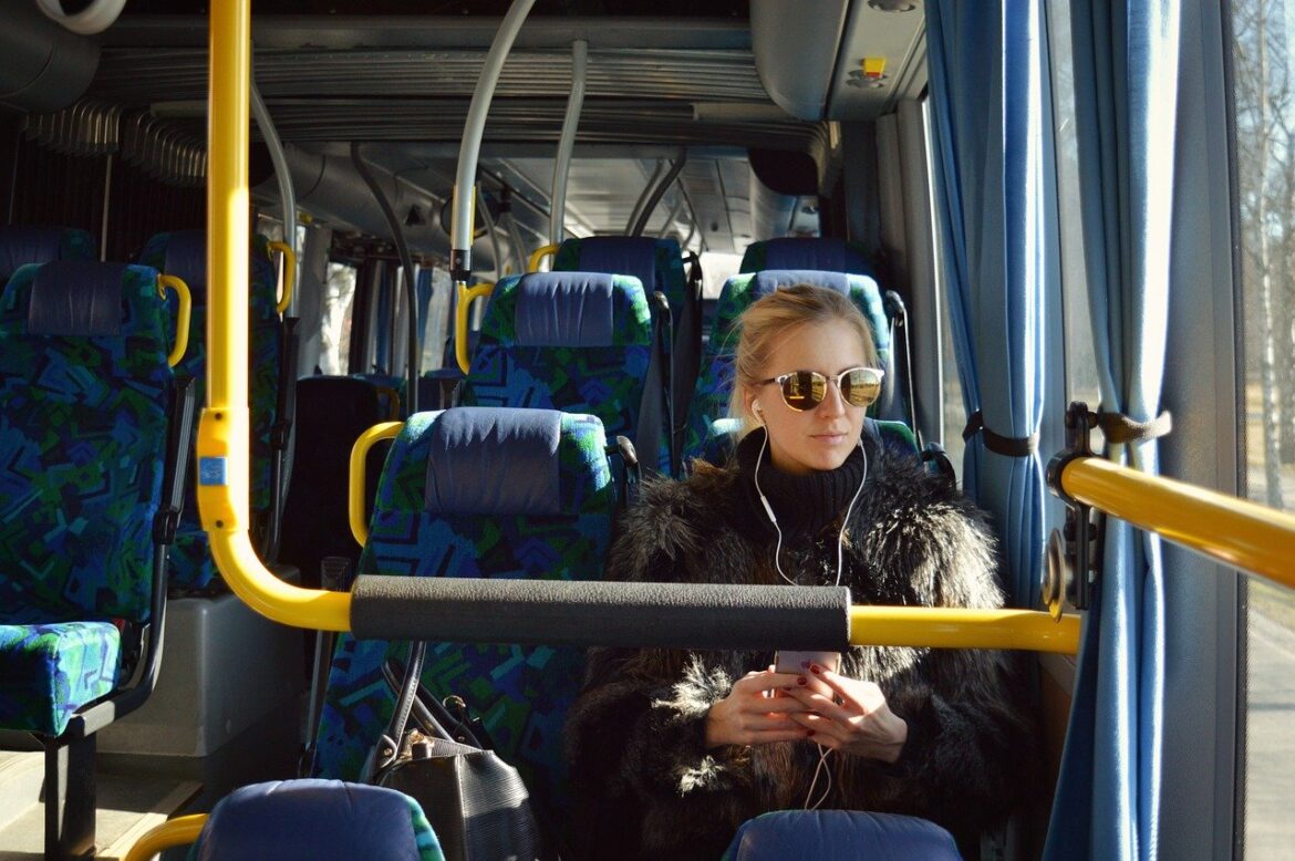 Frau mit Sonnenbrille sitzt in einem Bus und hört Musik.