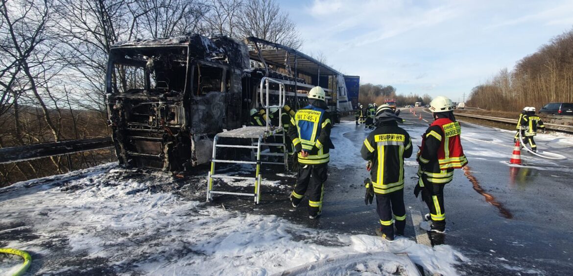 Feuerwehrleute löschen einen ausgebrannten LKW auf der Autobahn.