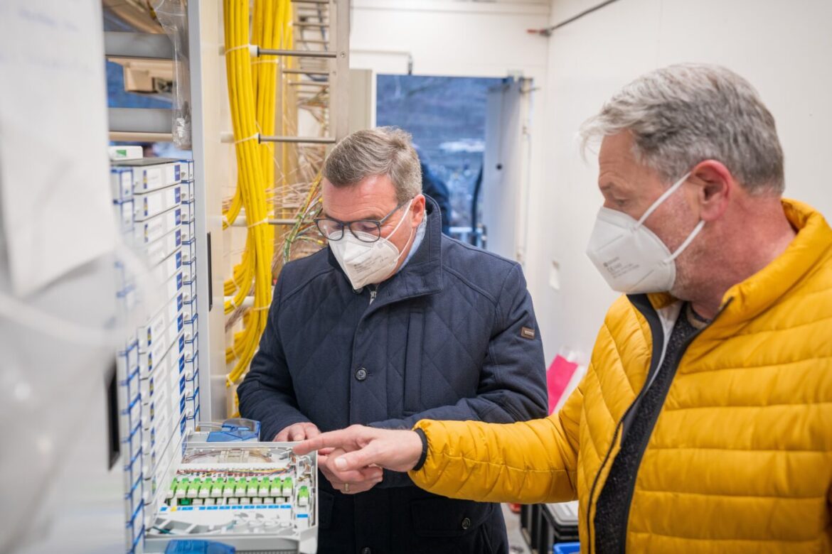 Zwei Männer mit Masken arbeiten an Glasfasertechnik.