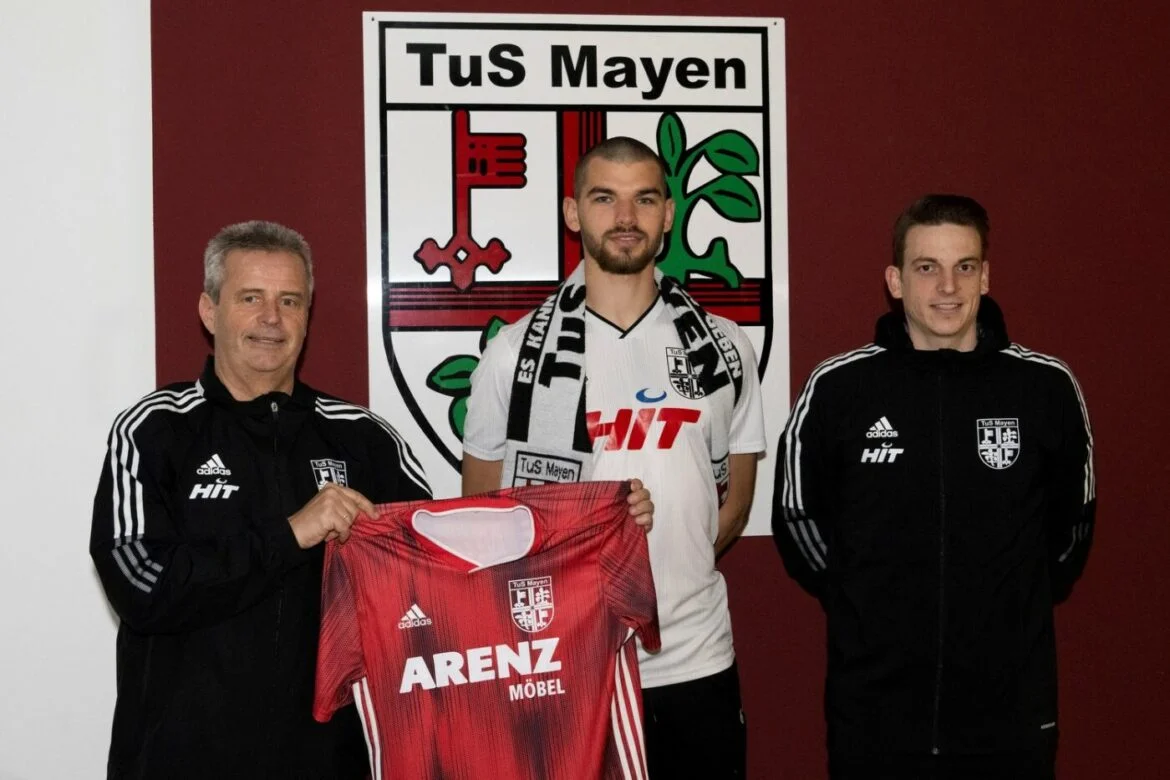 Drei Männer präsentieren ein Fußballtrikot von TuS Mayen.