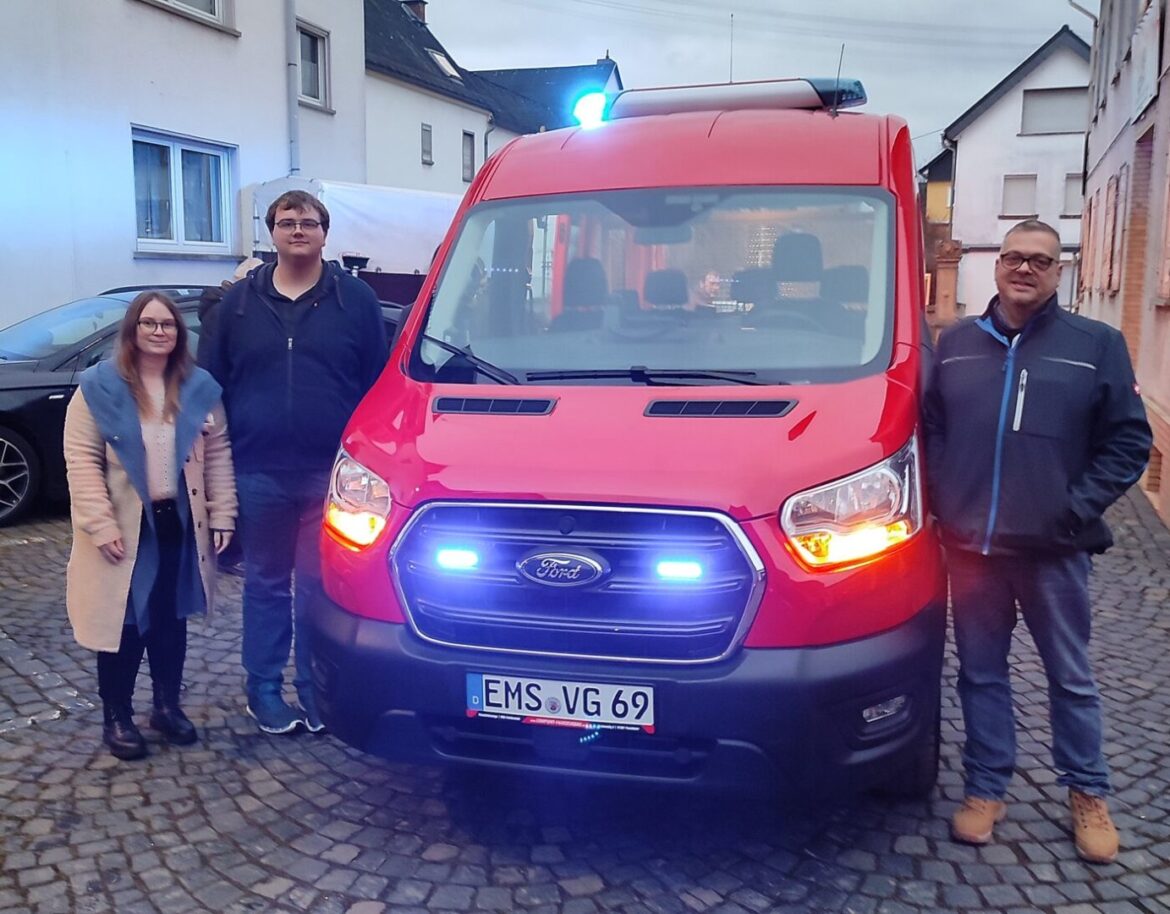 Rotes Einsatzfahrzeug mit drei Personen davor.