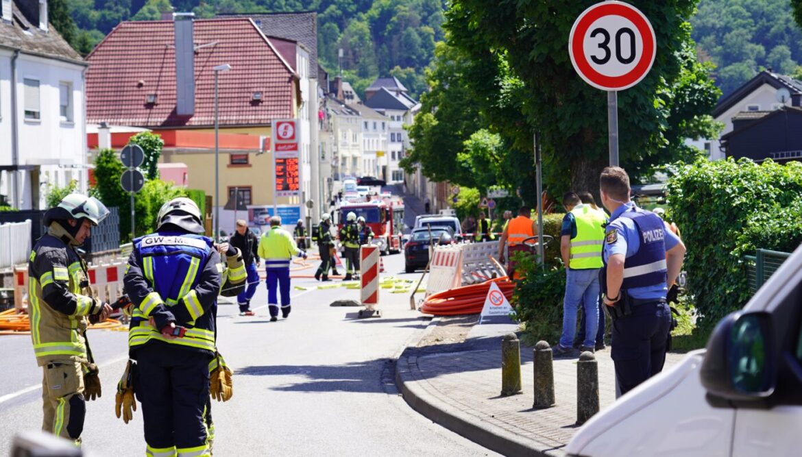 Einsatzkräfte, darunter Feuerwehr und Polizei, arbeiten an einer Baustelle in einer Ortsstraße. Verkehrsschilder und Absperrungen sind sichtbar.