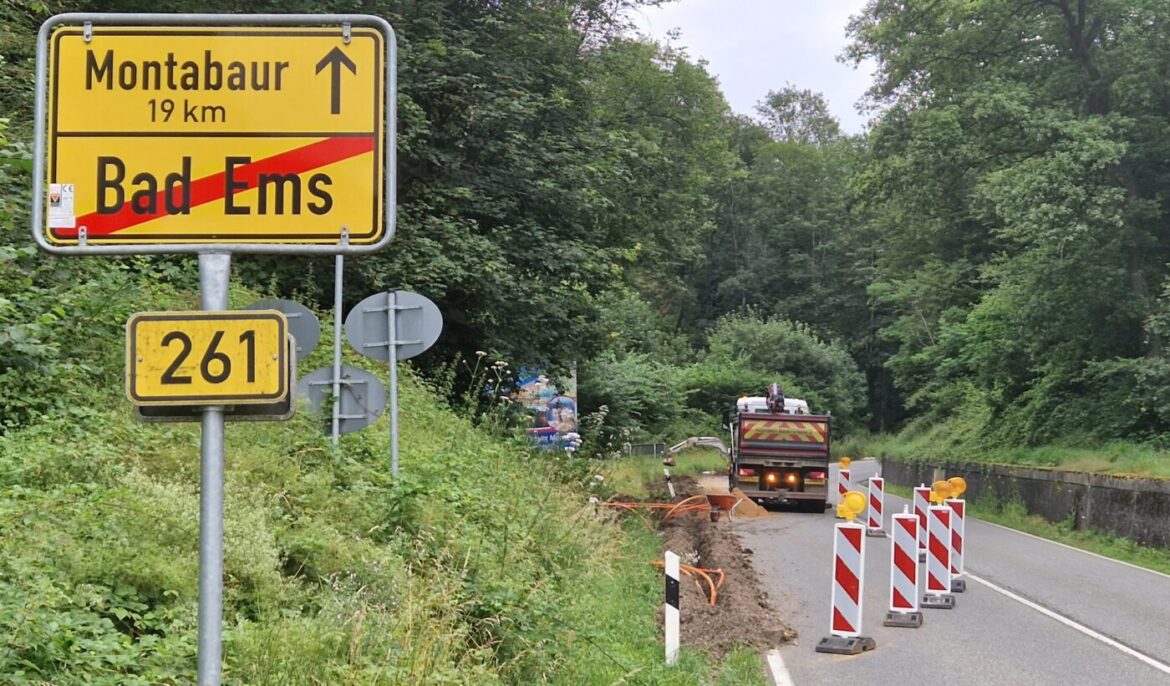 Ortsschild für Montabaur mit Entfernung, Bad Ems durch rote Linie durchgestrichen, Baustelle und Baustellenfahrzeug sichtbar.