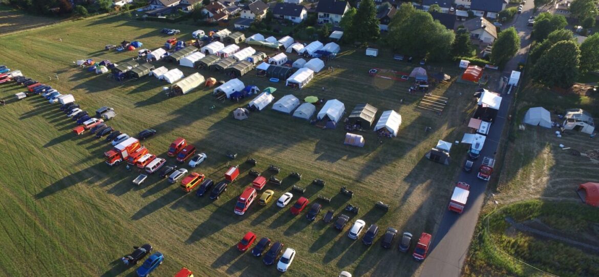 Luftaufnahme eines Campingplatzes mit Zelten und parkenden Fahrzeugen in einer offenen Landschaft.
