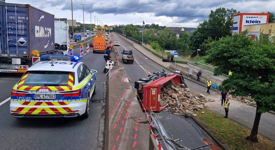 Ein umgekipptes Fahrzeug mit Schutt auf der Straße, Polizei und Rettungsdienste sind an der Unfallstelle.