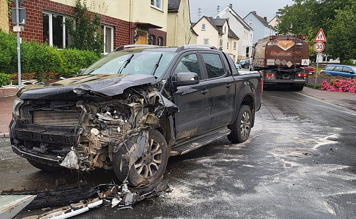 Ein beschädigter schwarzer Pickup steht auf der Straße, daneben ein Müllfahrzeug. Besondere Fokus auf die schwere Frontschäden.