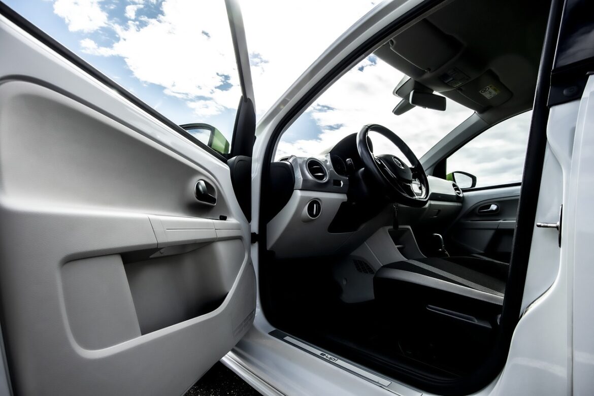 Innenansicht eines weißen Autos mit geöffnetem Tür und Blick auf das Lenkrad und Armaturenbrett.