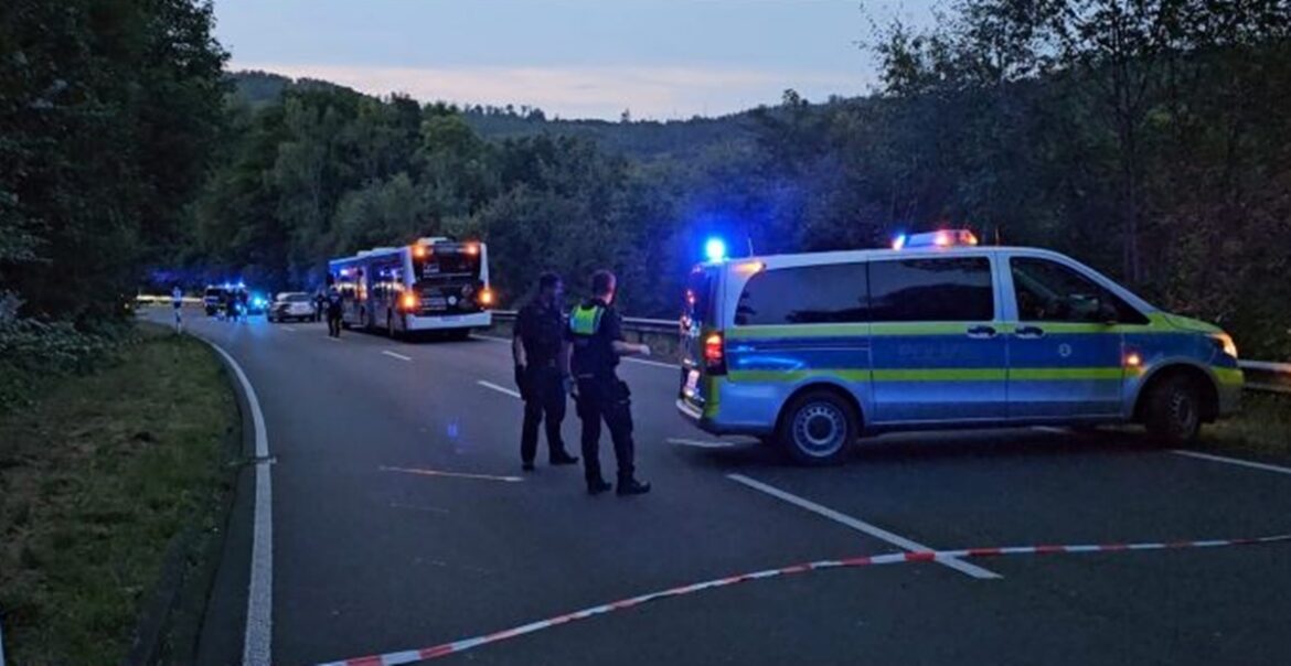 2024-08-30_Siegen_Eiserfeld_Messerstecherei_Bus_c_Ls Polizeifahrzeuge und Einsatzkräfte sichern eine Straße. Blaulicht leuchtet, Bäume im Hintergrund.