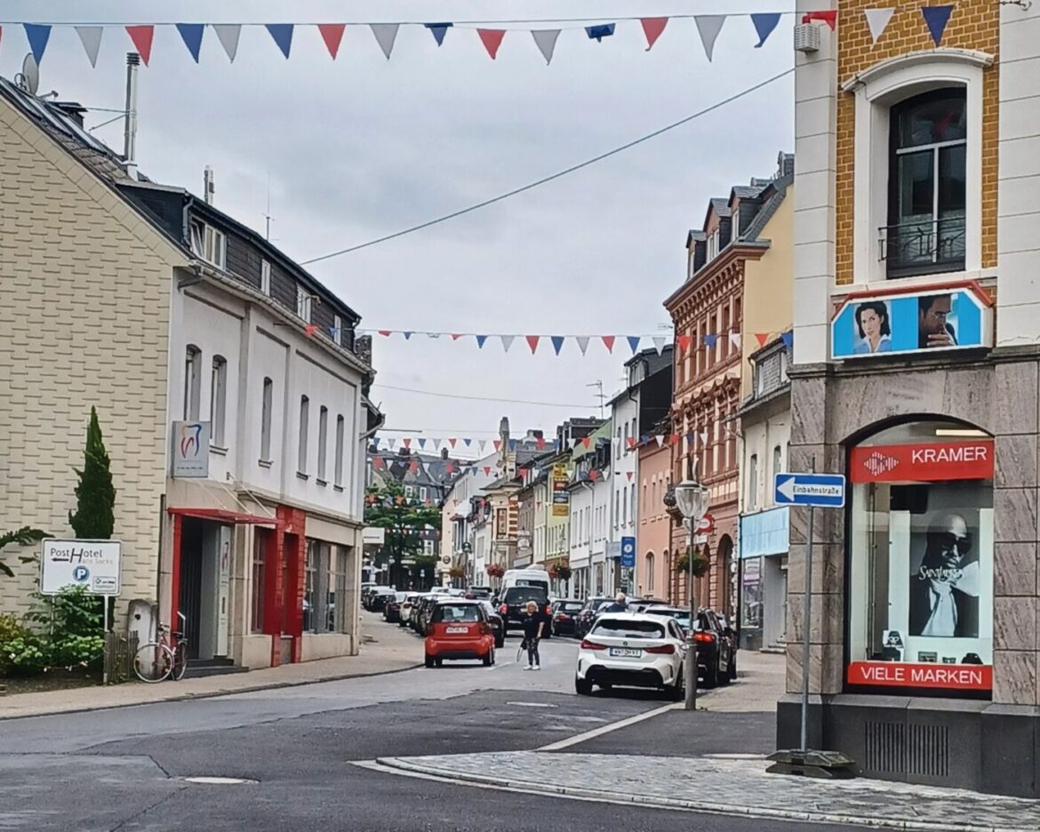 Bunte Wimpel hängen über einer Straßenansicht mit Autos, Geschäften und einem Hotel.