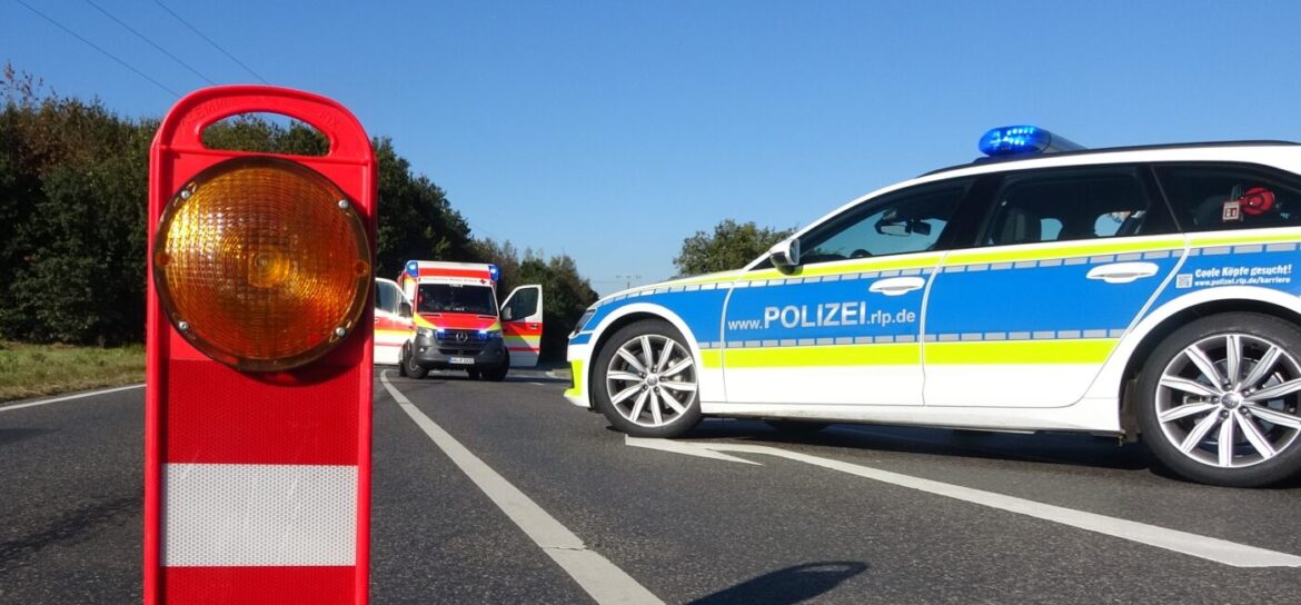 Polizeiwagen und Krankenwagen auf einer Straße, mit einer roten Warnleuchte im Vordergrund.