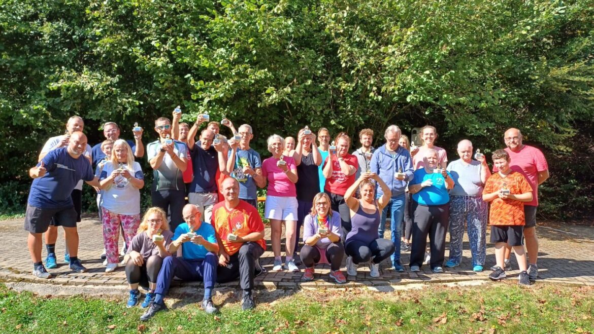 Eine Gruppe von 30 Personen steht im Freien und hält Medaillen in den Händen.