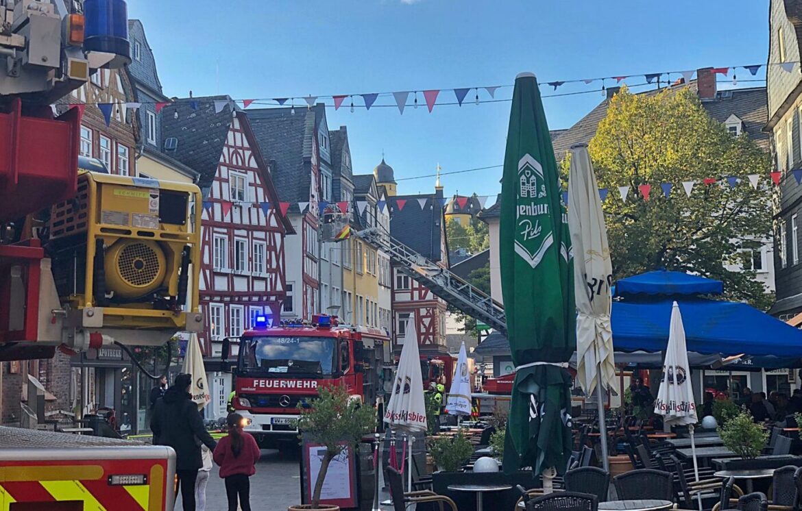 Feuerwehrfahrzeuge in einer Stadt mit historischen Gebäuden, Tischen und Stühlen unter Sonnenschirmen.