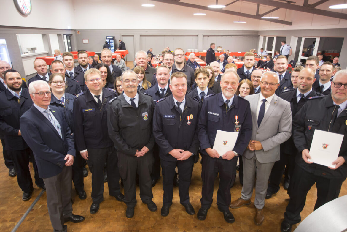 Gruppennahaufnahme von Feuerwehrleuten und Offiziellen bei einer Zeremonie, mit Tischen im Hintergrund.