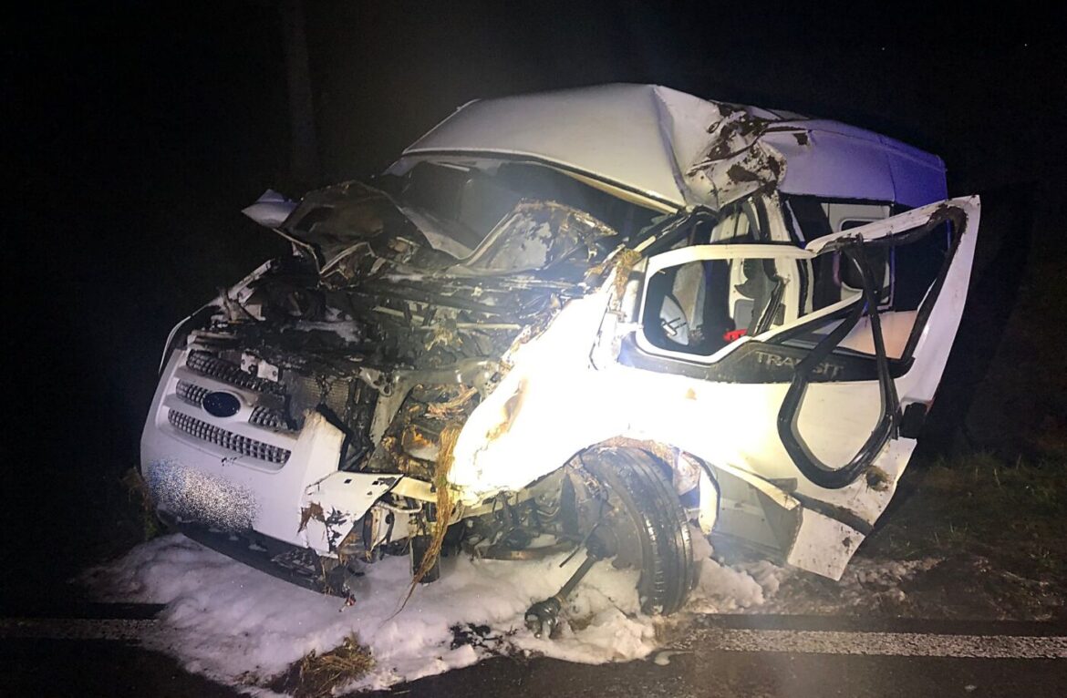 Unfallfahrzeug mit stark beschädigtem Vorderteil, Rauch und Schaum auf der Straße, dunkler Hintergrund.