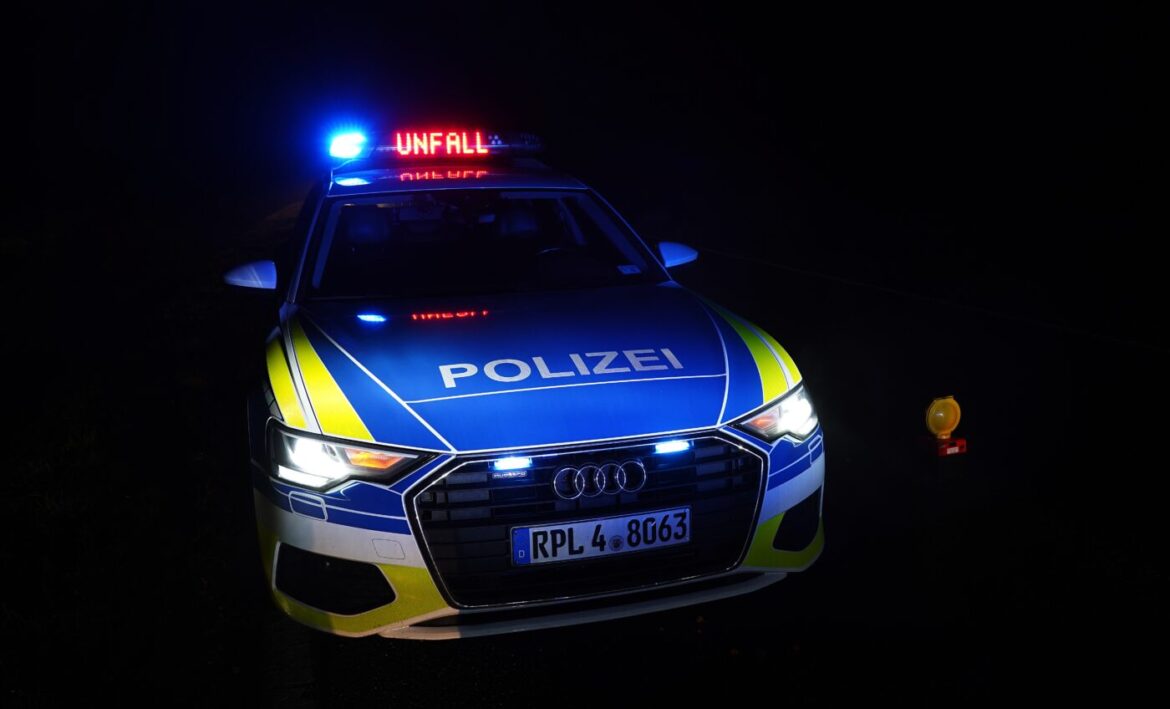 Polizeiauto bei Nacht, Blaulicht leuchtend, "Unfall" Zeichen, gelbe Warnleuchte am Straßenrand.